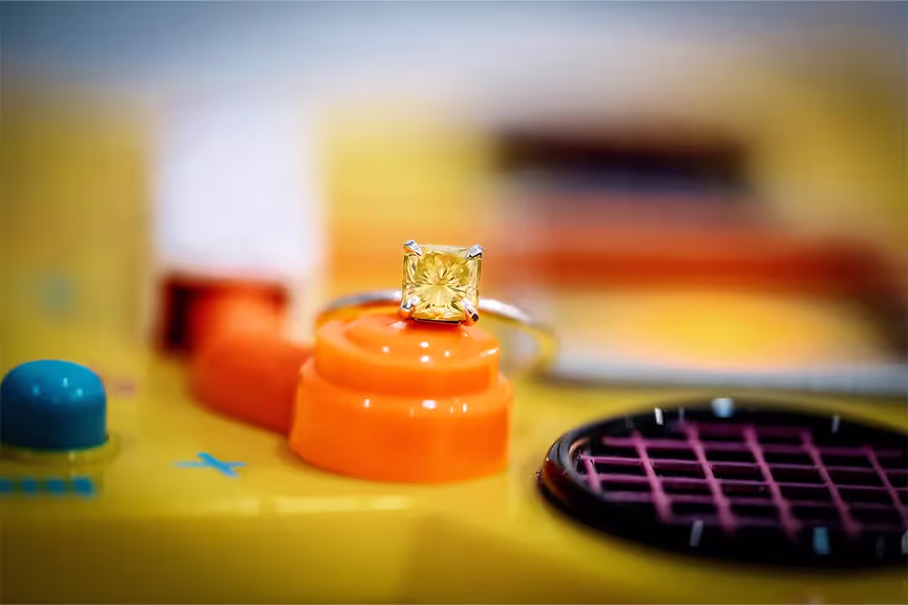 Yellow square-cut gemstone ring placed on an orange button of a yellow vintage electronic device with colorful buttons and speaker.