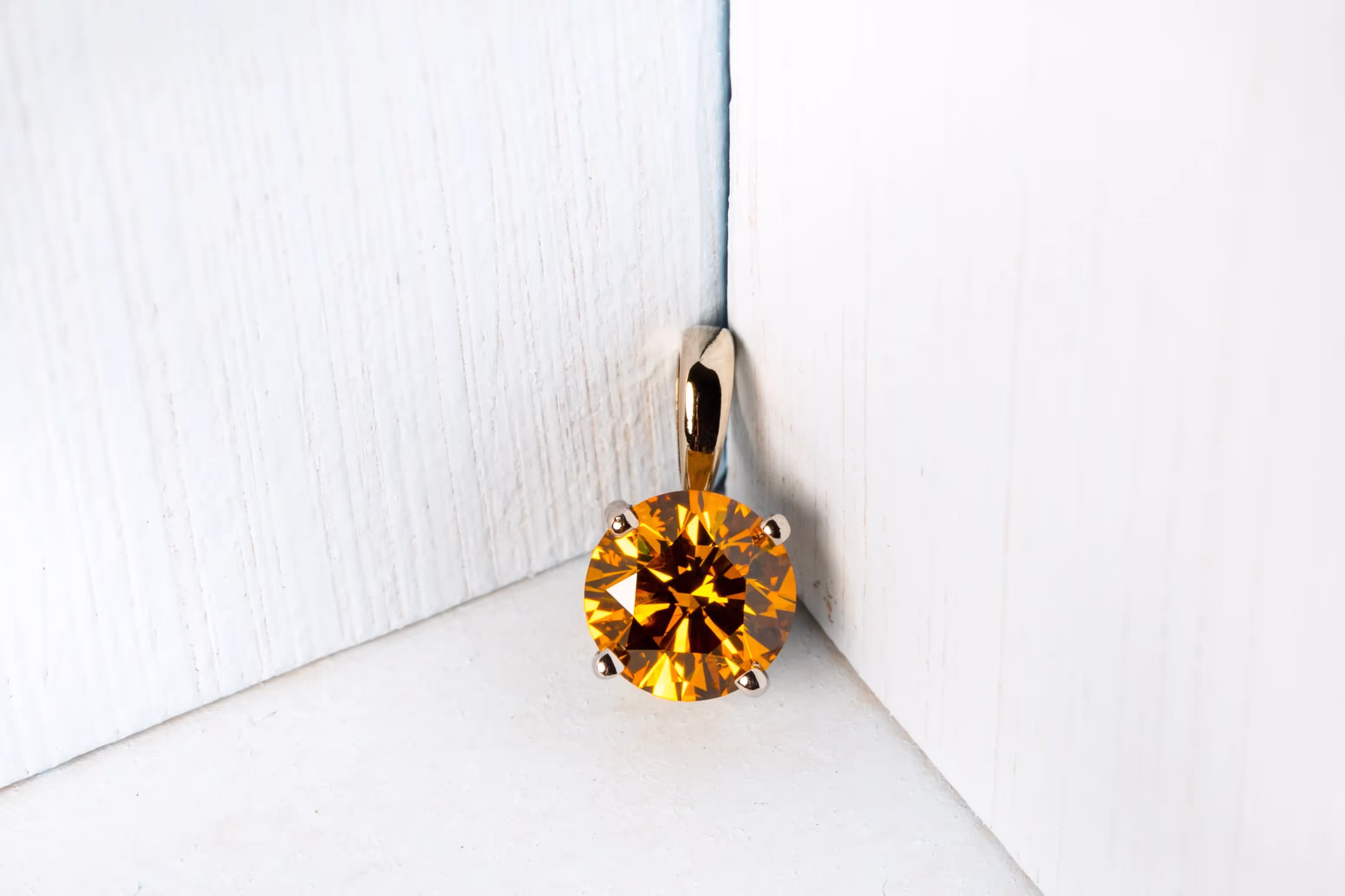 Round yellow-orange gemstone pendant with gold bail against a white wooden corner background.
