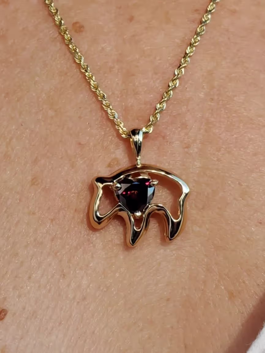 Gold necklace with a bear-shaped pendant featuring a dark red triangular gemstone in the center.