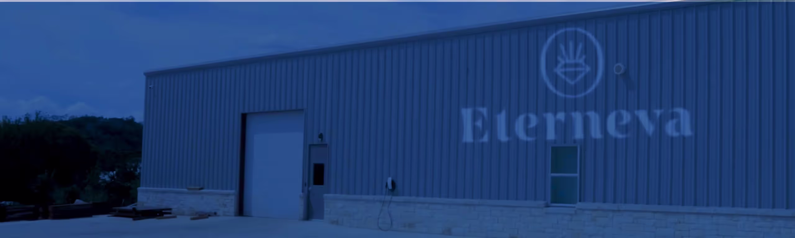 The exterior of Eterneva's Kerrville lab: a large metal building with a sliding door, set against trees and hills.