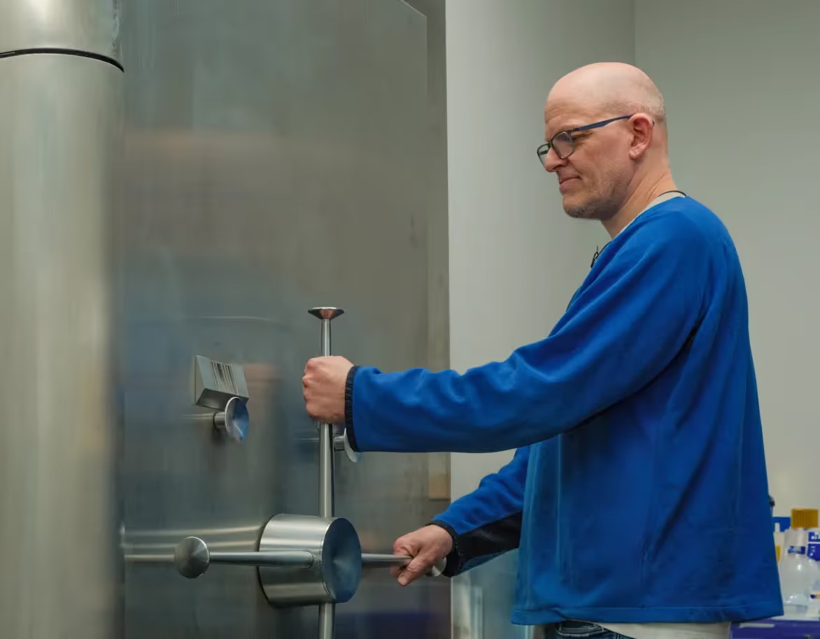 A man in a blue sweater opening a large stainless steel vault door.