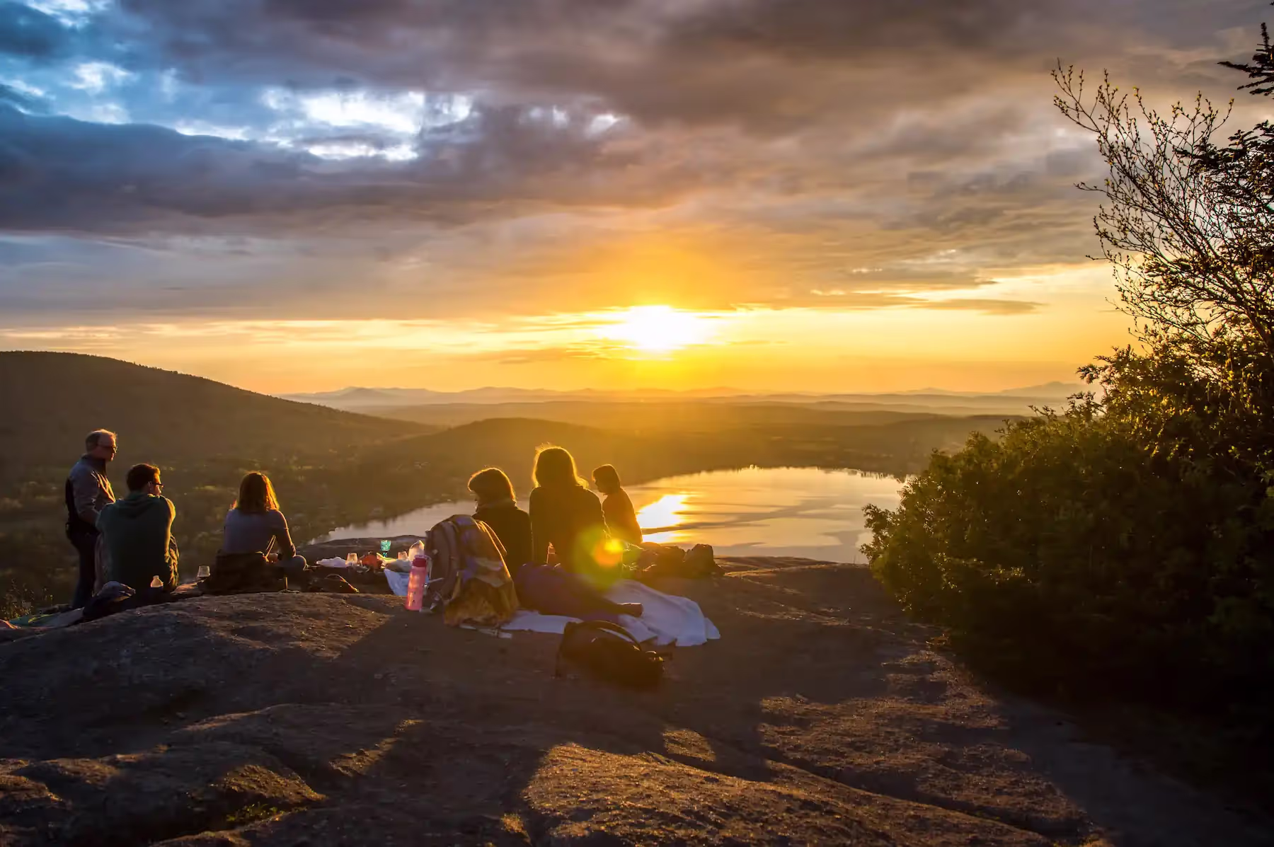Group of people watching the sun set on top of a mountain.
