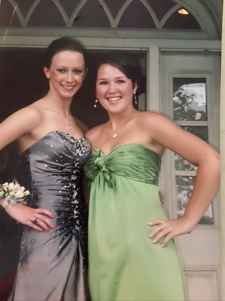 Two young women in formal gowns posing together outside a doorway.