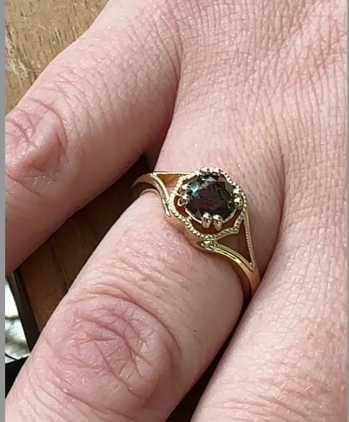 female hand wearing gold band with red diamond