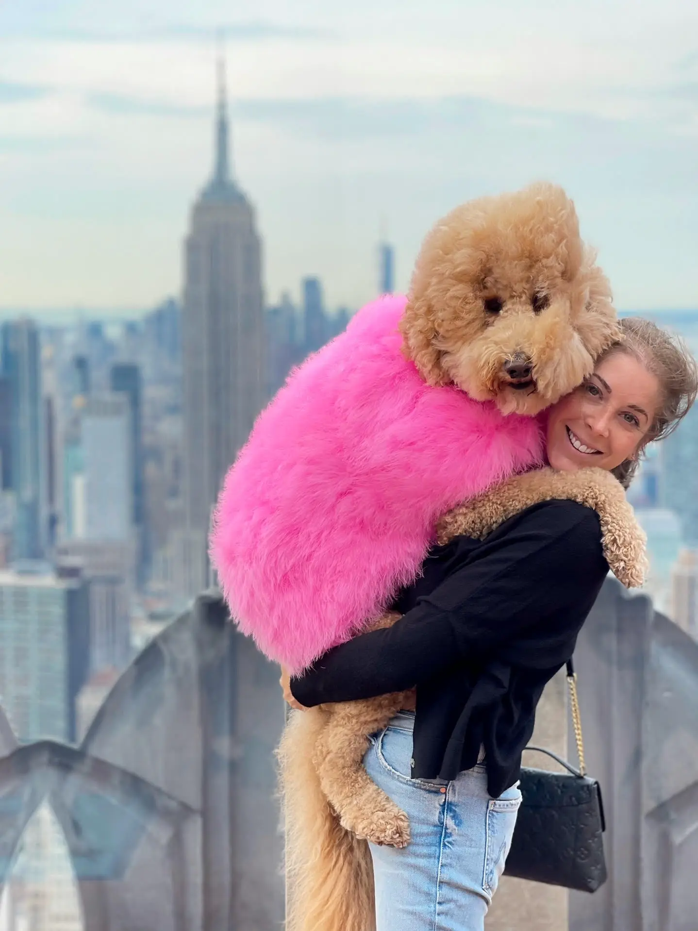Paige hugging Sawyer, dressed in a fluffy pink sweater, in front of the Empire State Building