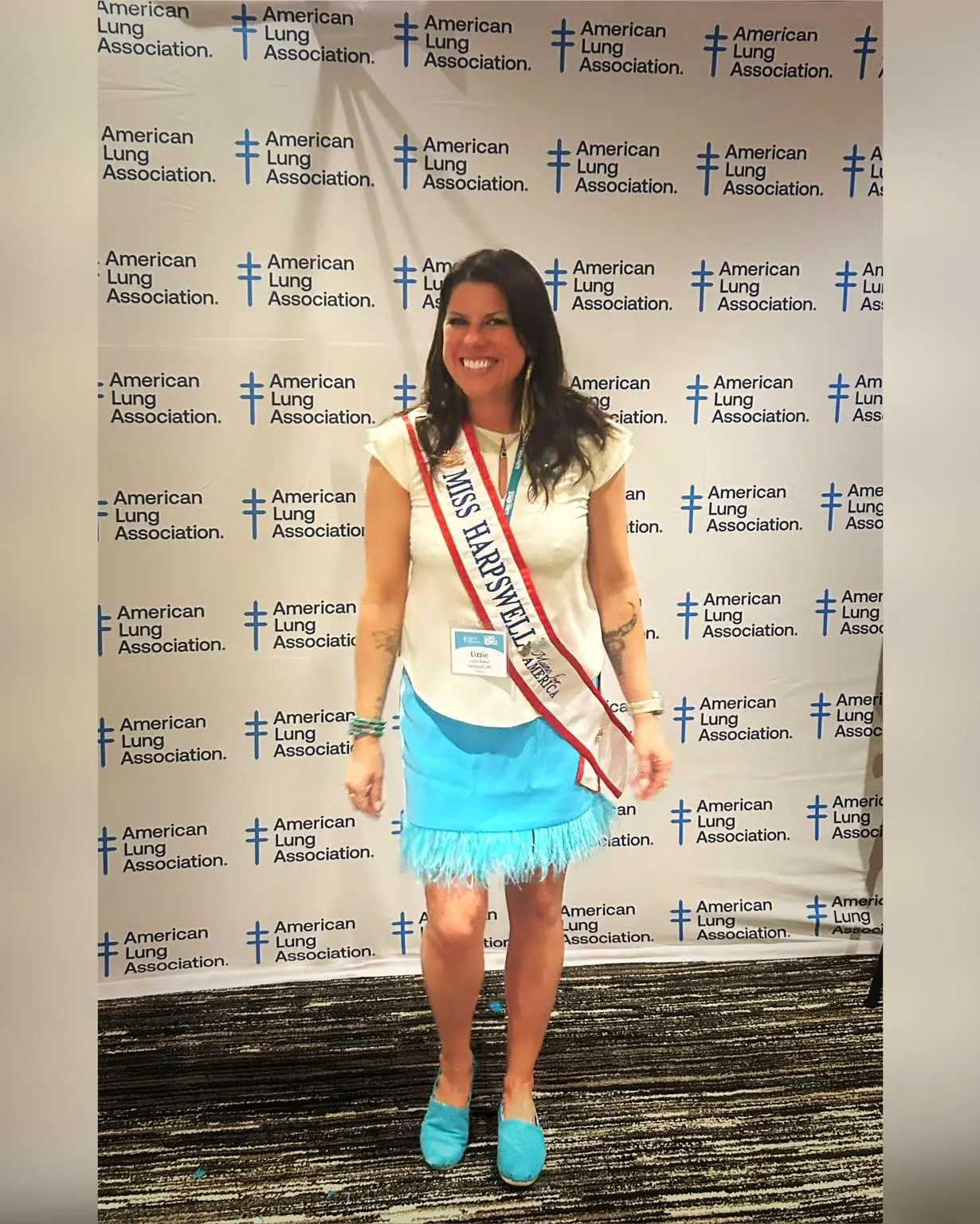 Lizzie wearing a pageant sash in front of an American Lung Association backdrop.