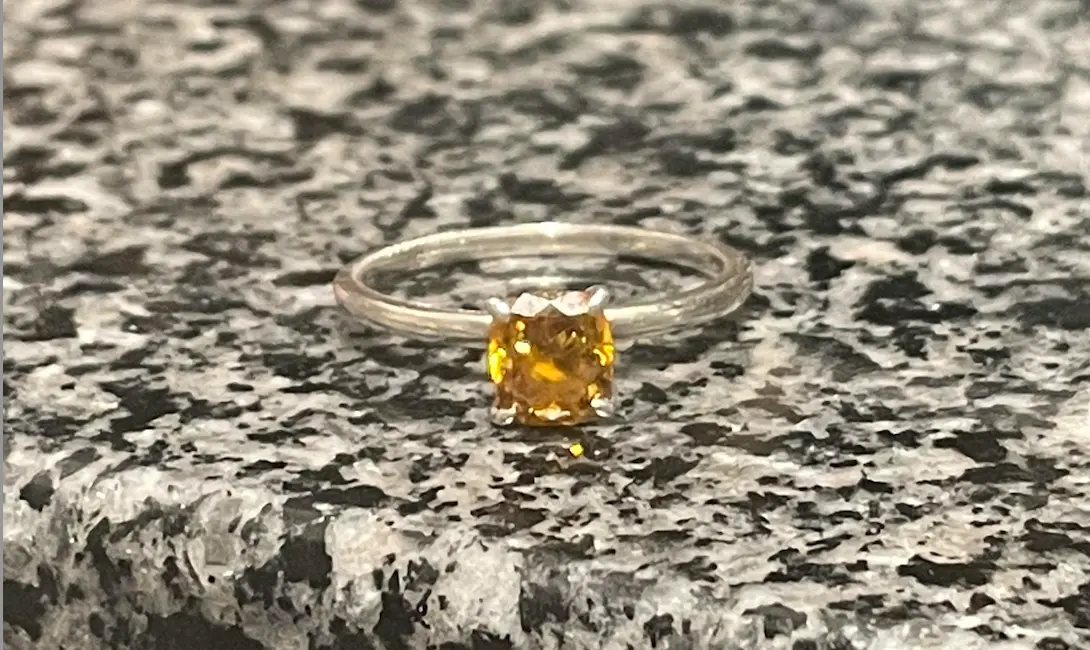 Silver ring with yellow diamond rests on granite countertop