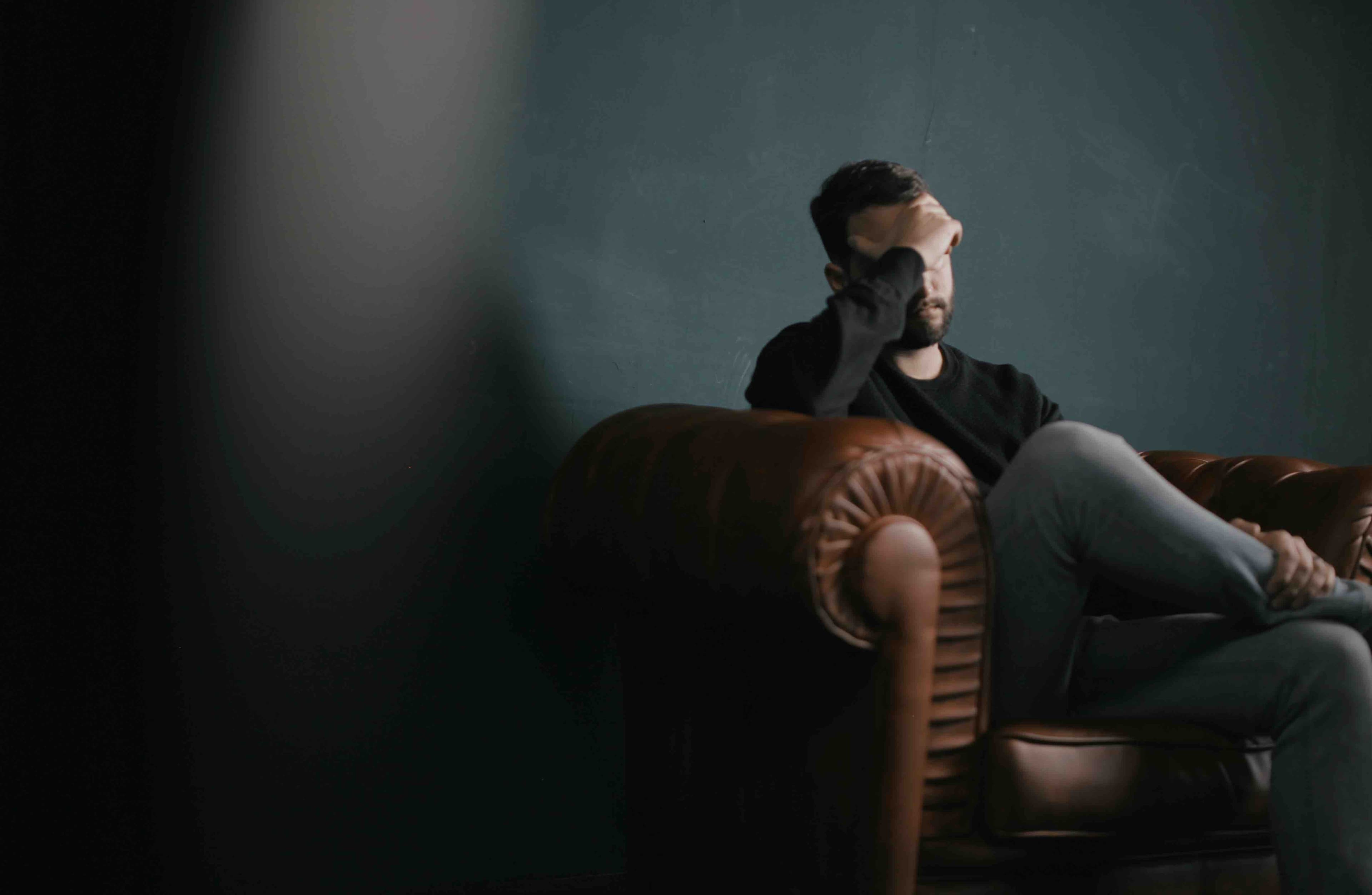 Man sitting alone on a leather couch with his hand over his face
