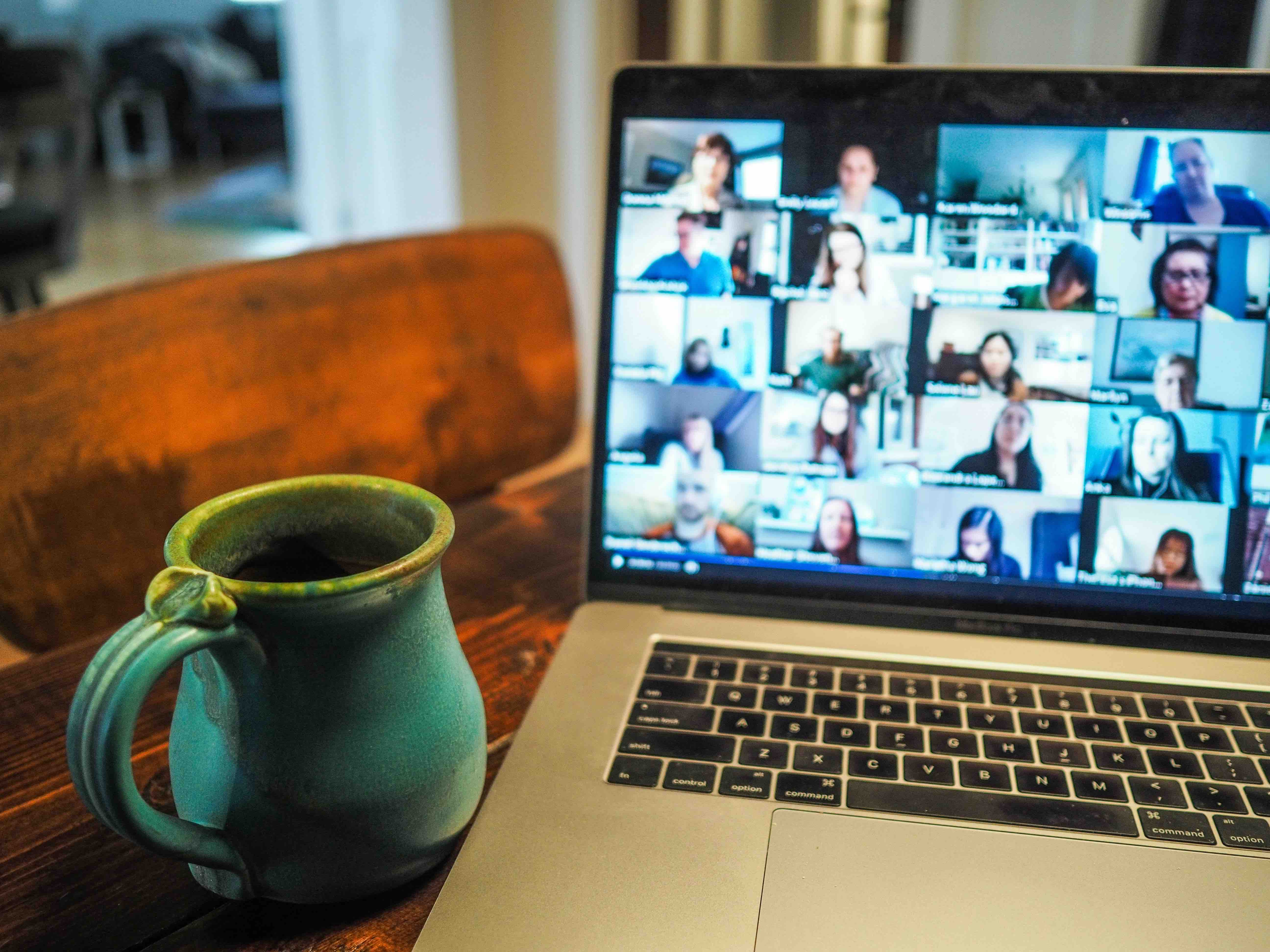 Laptop showing a video call grid of support group members beside a coffee mug