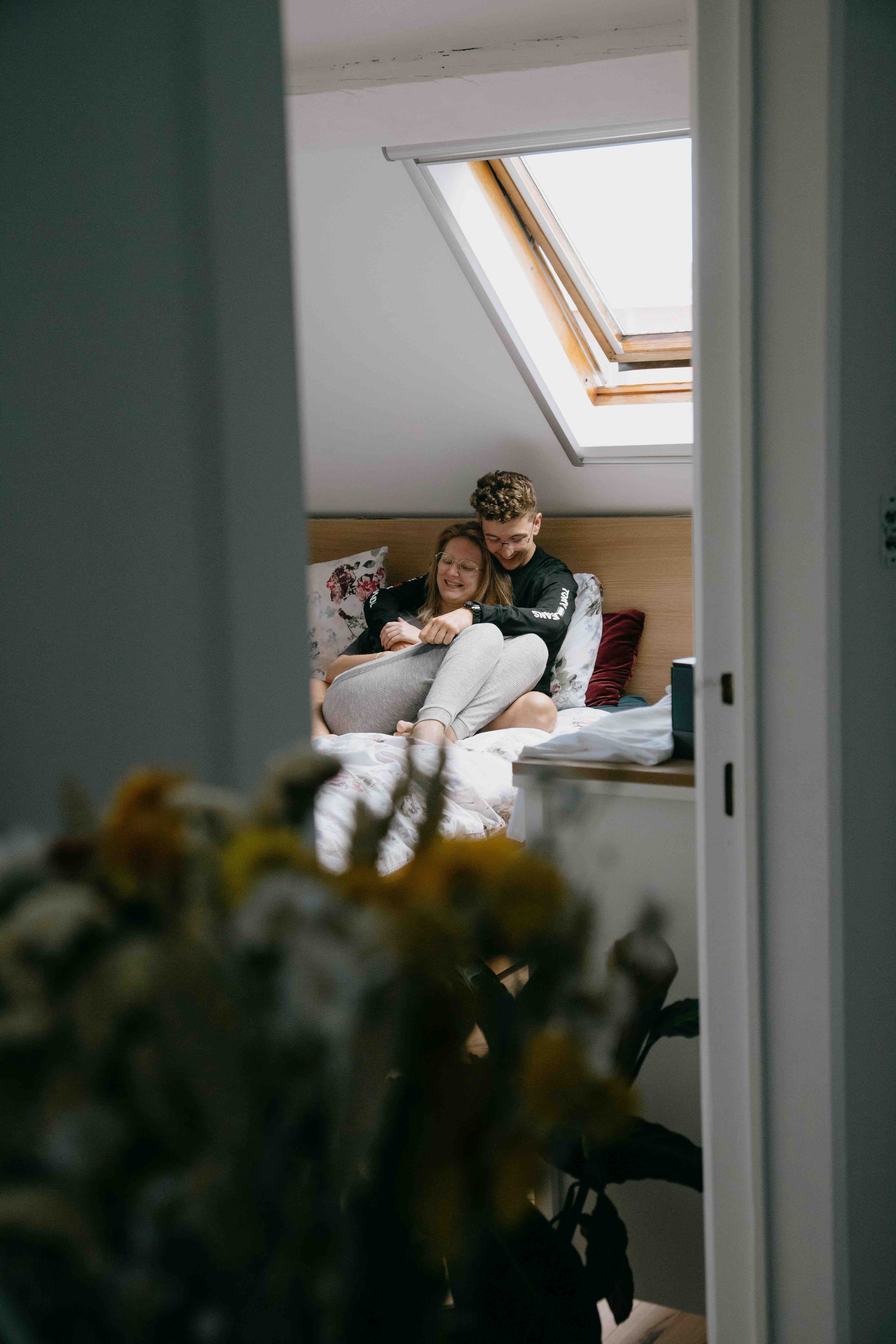 Couple cuddling and talking on a bed, seen through a doorway